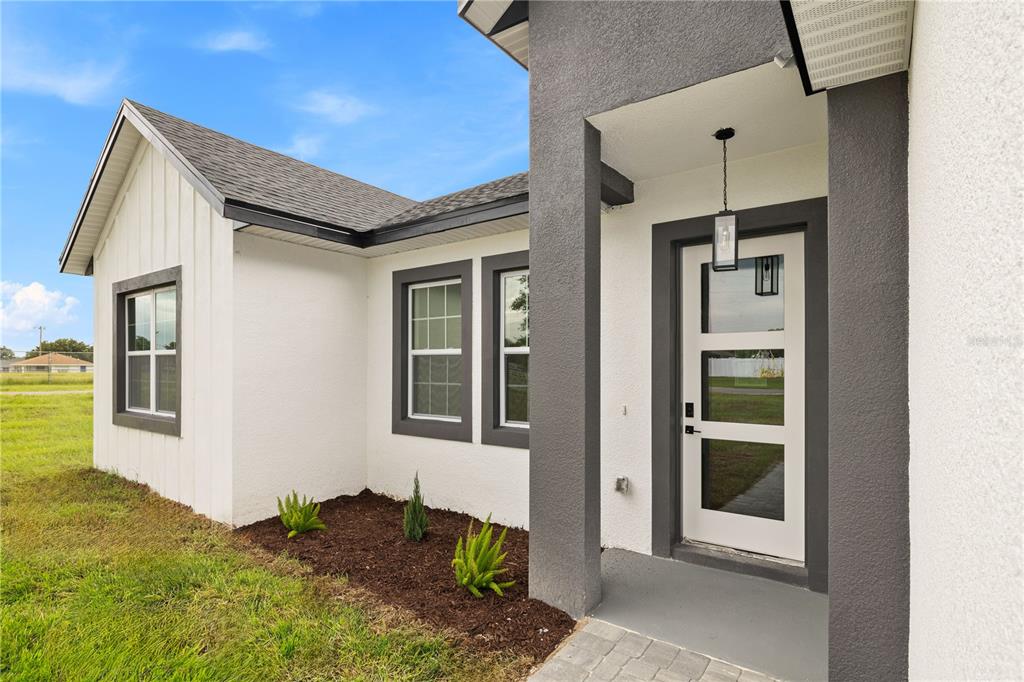 A modern home exterior features white board-and-batten siding, dark gray trim, and a glass-paneled front door — 14144 SW 47 AVENUE, OCALA, FL