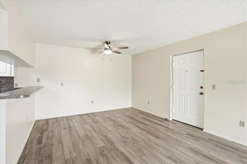 An empty room features light-colored walls, wood-look flooring, a ceiling fan, and an entry door — 1515 FORREST NELSON BOULEVARD UNIT B206, PORT CHARLOTTE, FL