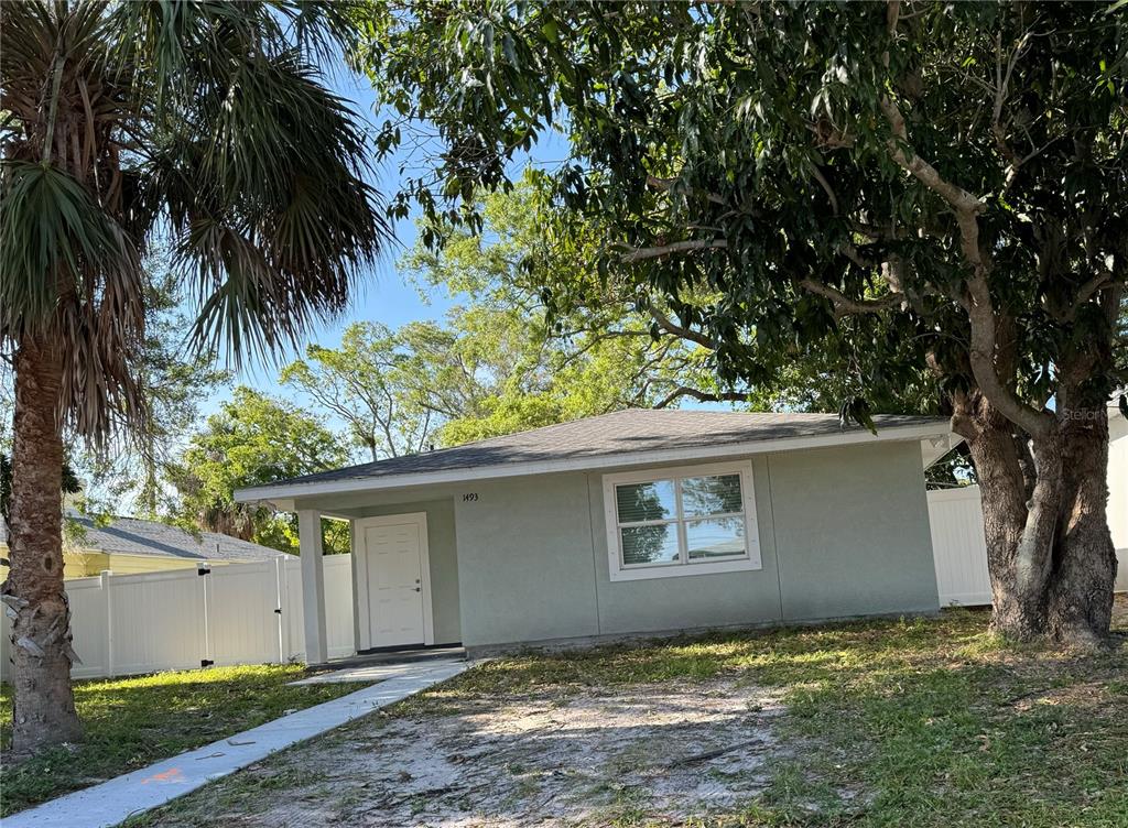 A light green single-story house with a white door and a large tree in front — 1493 CLEVELAND STREET, CLEARWATER, FL