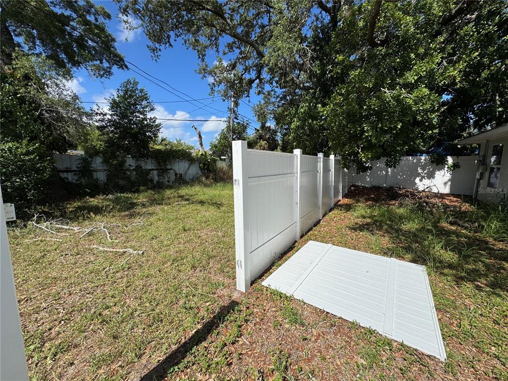 A white vinyl fence stands in a grassy backyard with trees and a detached panel — 1493 CLEVELAND STREET, CLEARWATER, FL
