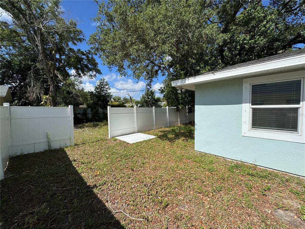 A backyard with a white vinyl fence, a small concrete pad, and a light blue house — 1493 CLEVELAND STREET, CLEARWATER, FL