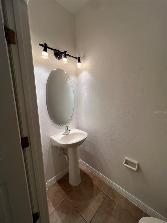 A small powder room features a pedestal sink, an oval mirror, and industrial-style lighting — 7523 PELLHAM WAY, KISSIMMEE, FL