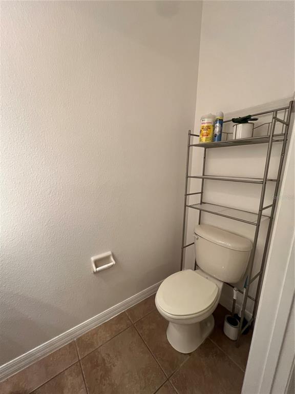 A bathroom features a toilet with an over-the-toilet metal storage rack and tiled flooring — 7523 PELLHAM WAY, KISSIMMEE, FL