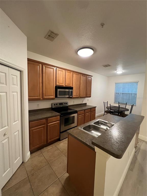 A kitchen features wood cabinets, stainless steel appliances, a center island, and tile flooring — 7523 PELLHAM WAY, KISSIMMEE, FL