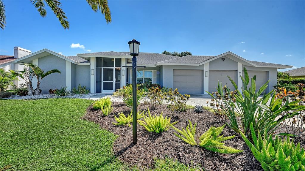 A single-story house with a gray exterior, three-car garage, and a landscaped front yard — 6988 COUNTRY LAKES CIRCLE, SARASOTA, FL