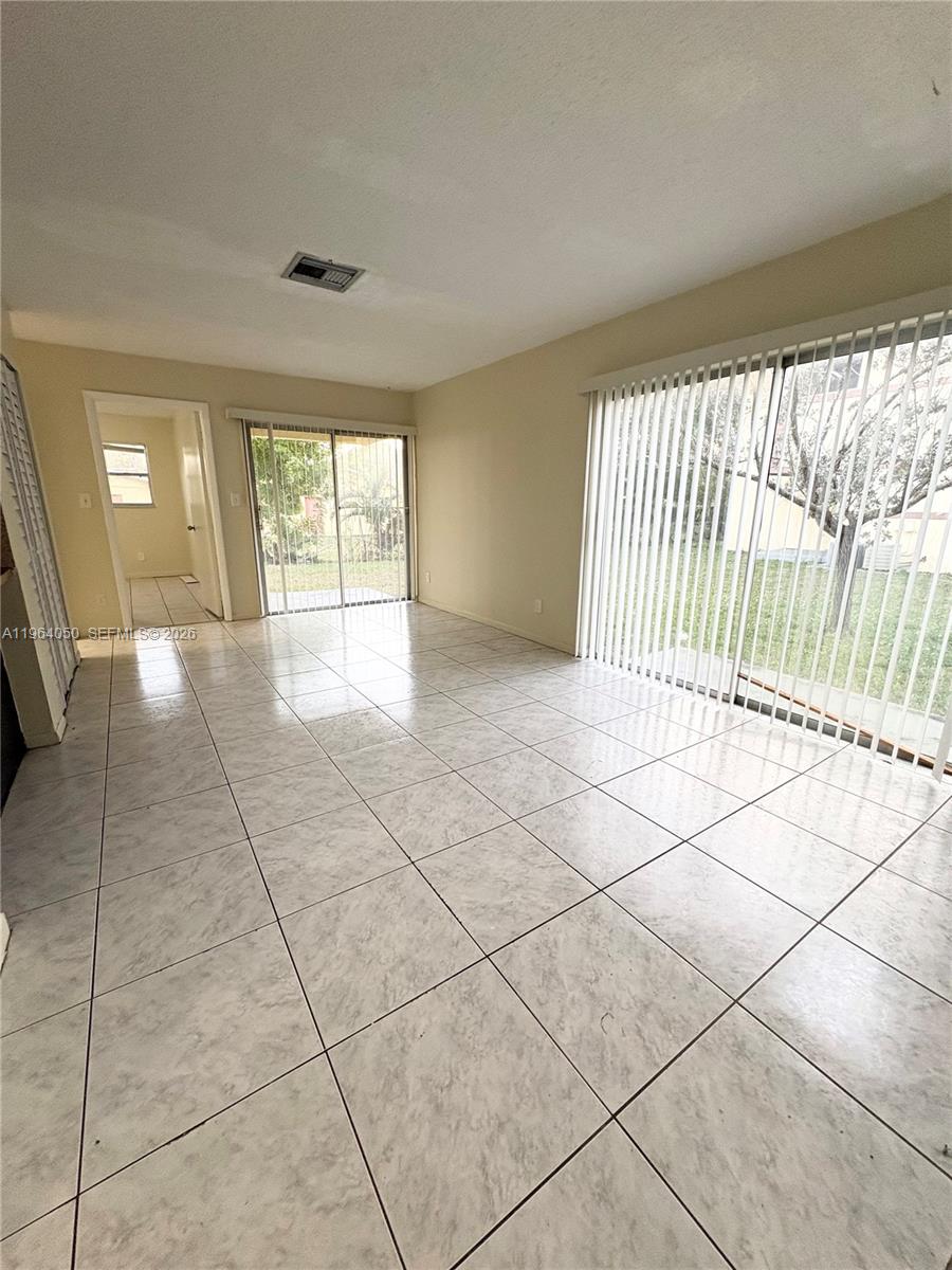 An empty room features light-colored tile flooring, white walls, and two sets of sliding glass doors — 813 SW 10th St # B, Hallandale Beach FL 33009, HALLANDALE BEACH, FL