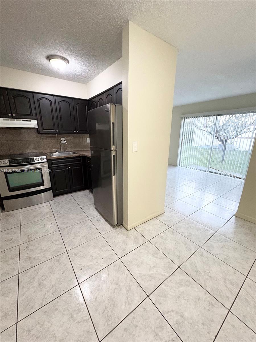 A kitchen with dark cabinets and stainless steel appliances opens to a tiled dining area — 813 SW 10th St # B, Hallandale Beach FL 33009, HALLANDALE BEACH, FL
