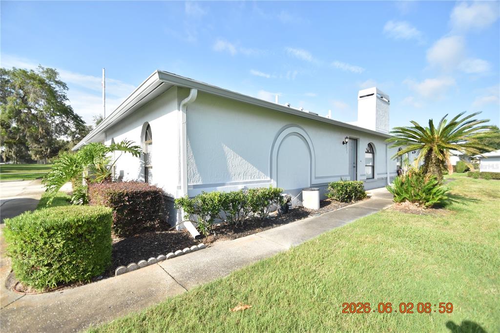 A side exterior view of a white house with a chimney and a concrete walkway — 23223 CLUB VILLAS DRIVE UNIT 23223, LAND O LAKES, FL