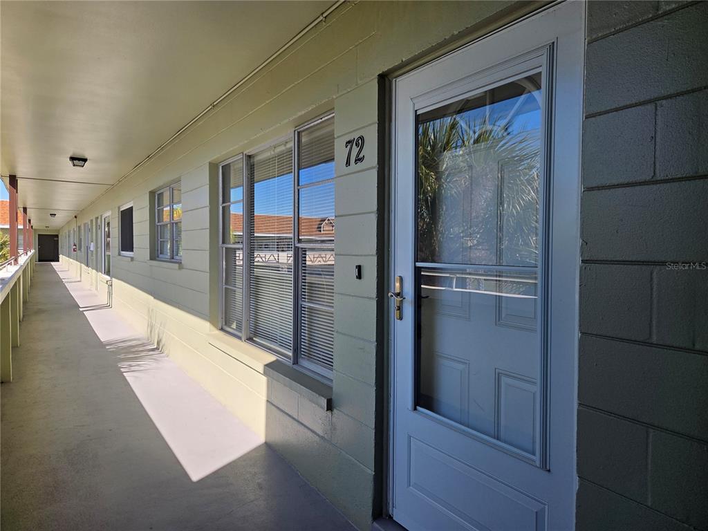 An exterior walkway of a multi-unit building features a numbered door and several windows — 2448 COLUMBIA DRIVE UNIT 72, CLEARWATER, FL