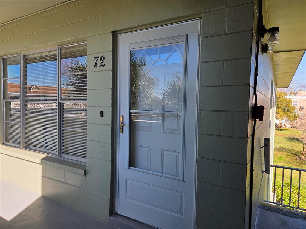 A light green exterior wall features a white storm door and the number 72 — 2448 COLUMBIA DRIVE UNIT 72, CLEARWATER, FL