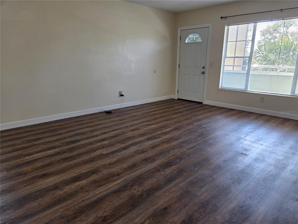 An empty room features wood-look laminate flooring, beige walls, a white entry door, and a window — 2448 COLUMBIA DRIVE UNIT 72, CLEARWATER, FL