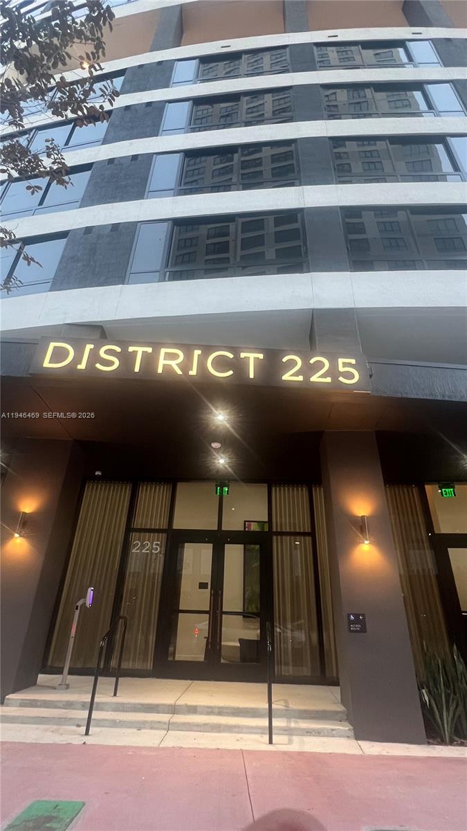 The exterior entrance of a modern multi-story building features glass doors and signage reading District 225 — 225 N Miami Ave # 905, Miami FL 33128, MIAMI, FL