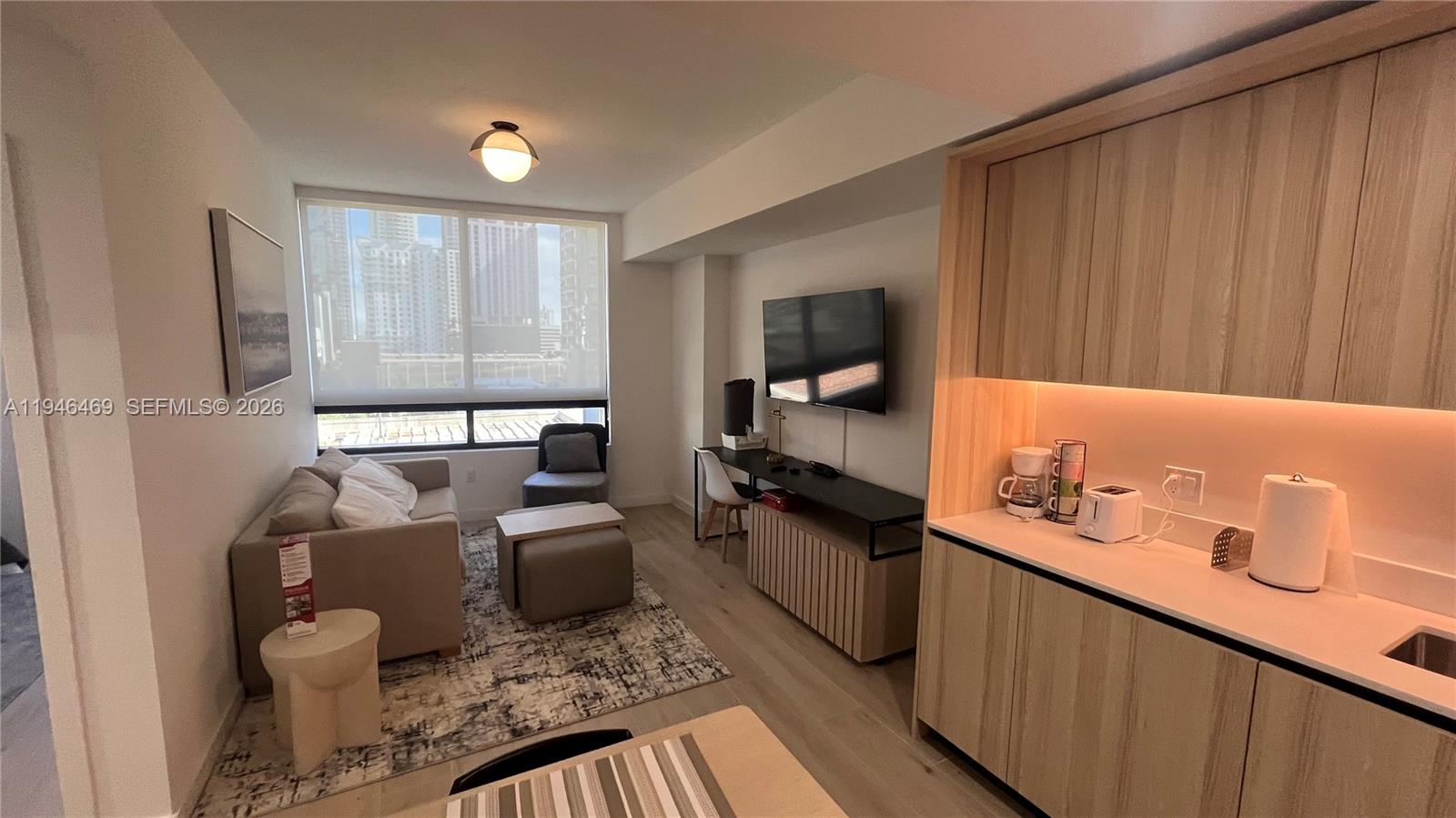 A modern studio apartment features a kitchenette, living area, and floor-to-ceiling windows with city views — 225 N Miami Ave # 905, Miami FL 33128, MIAMI, FL