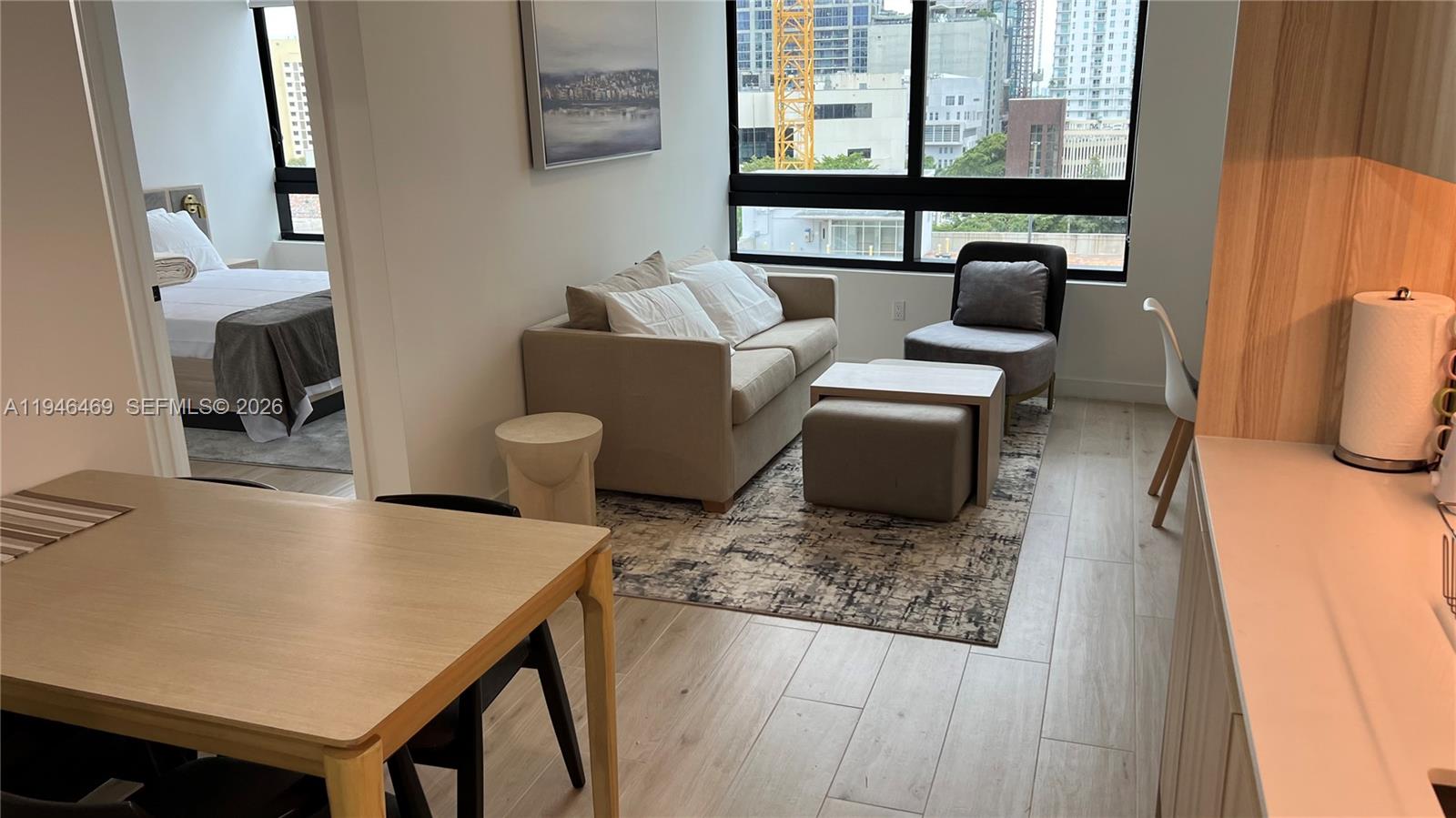A living area with a sofa, armchair, and dining table overlooks a city skyline — 225 N Miami Ave # 905, Miami FL 33128, MIAMI, FL