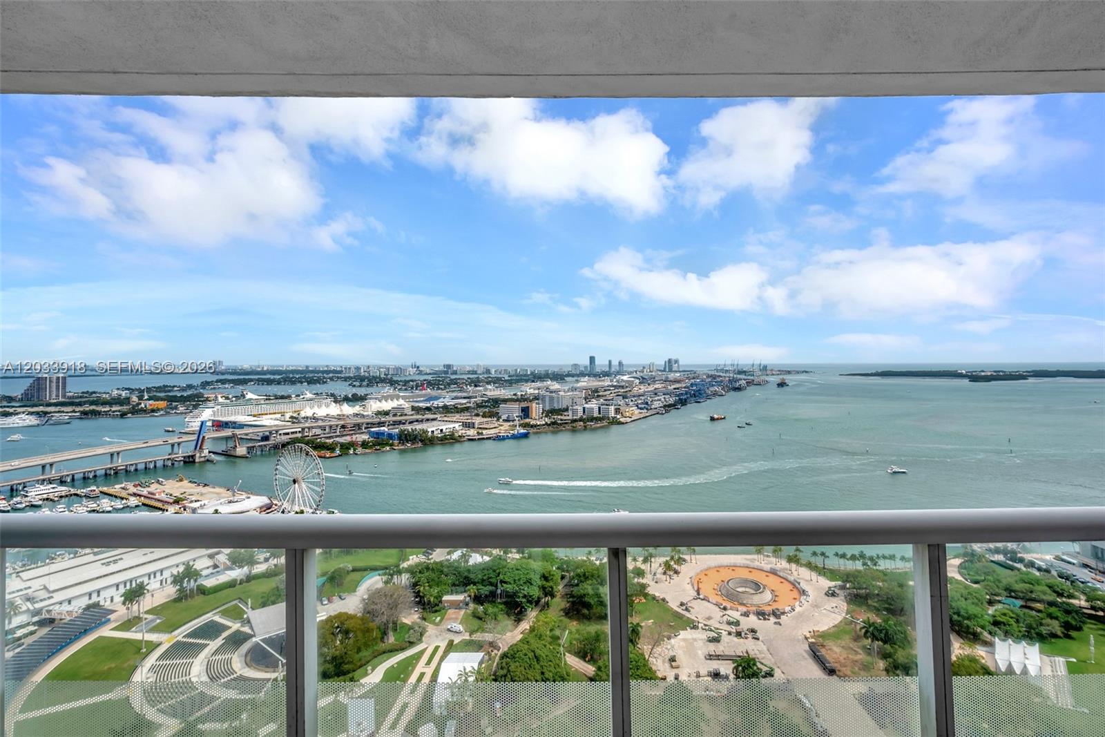 A high-angle view from a balcony overlooks a bay, a park, and a city skyline — 50 Biscayne Blvd # 3802, Miami FL 33132, MIAMI, FL