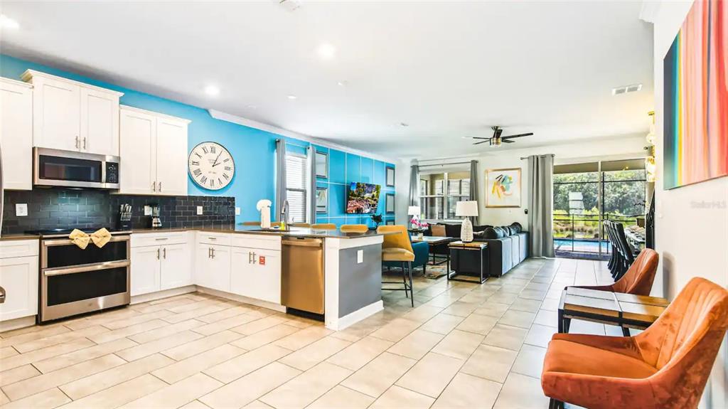 An open-concept kitchen and living area features white cabinetry, a bright blue wall, and tile flooring — 2965 PROTAGONIST STREET, KISSIMMEE, FL