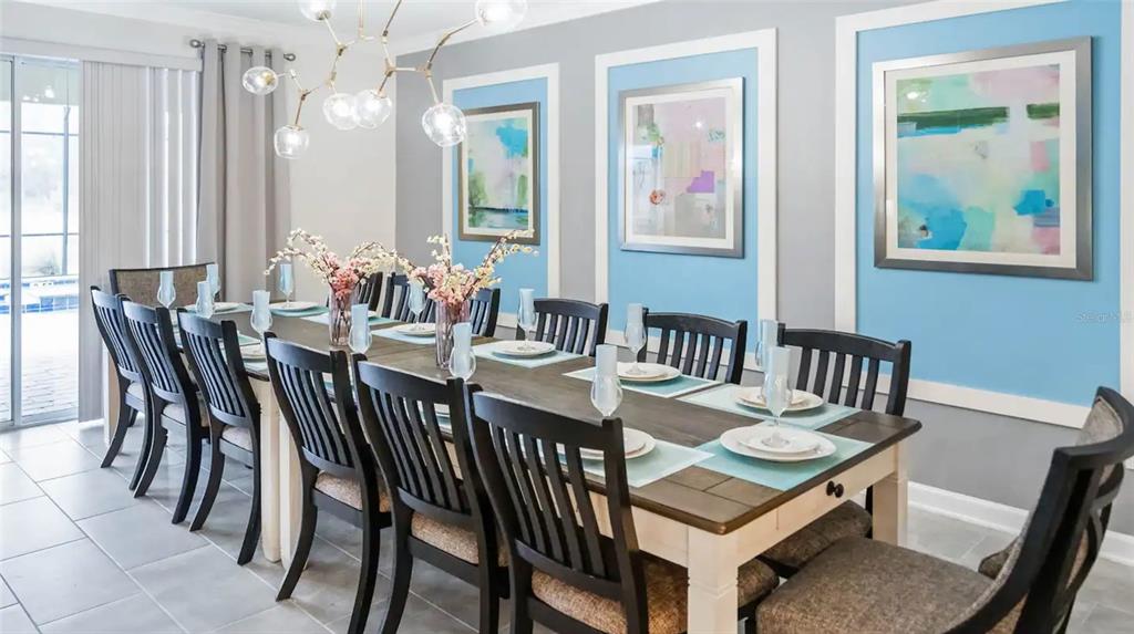 A dining room features a long wooden table, black chairs, and blue-framed wall art — 2965 PROTAGONIST STREET, KISSIMMEE, FL