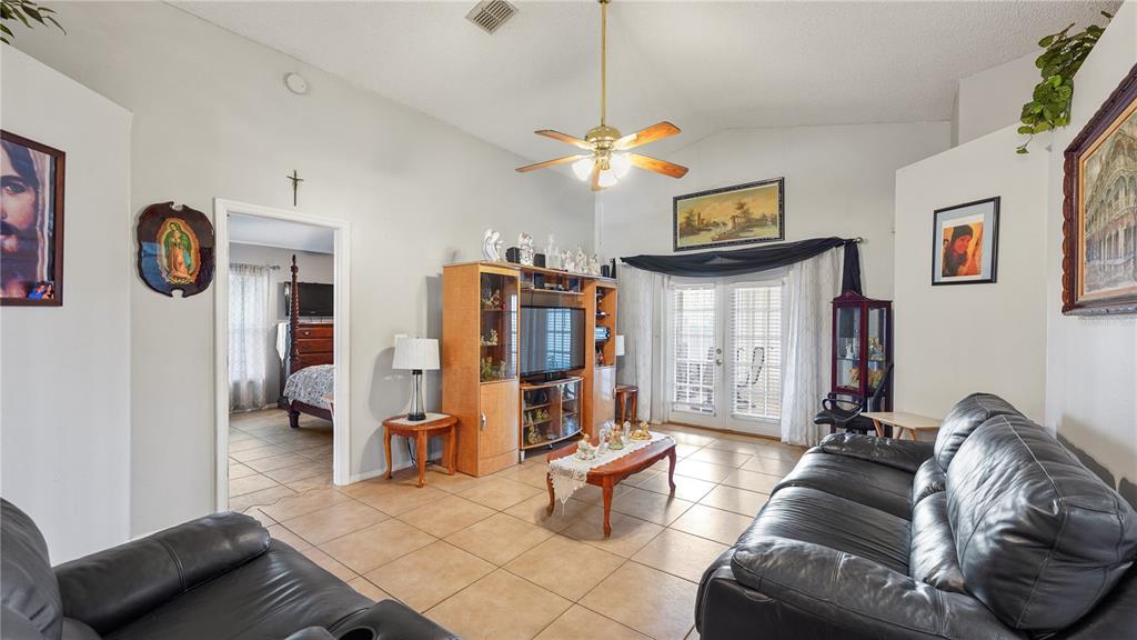A living room with tile floors, a ceiling fan, a leather sofa, and glass doors — 291 PINE ARBOR DRIVE, ORLANDO, FL