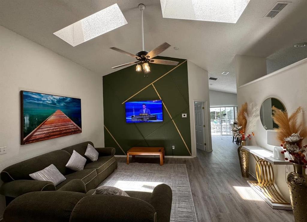 A living room features a green accent wall with gold trim, a sofa, and skylights — 121 BLOOMINGDALE DRIVE, DAVENPORT, FL