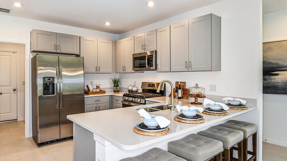 A modern kitchen with white cabinets, stainless steel appliances, and an island overlooks a living area — 13431 CAMELOT COURT, PARRISH, FL