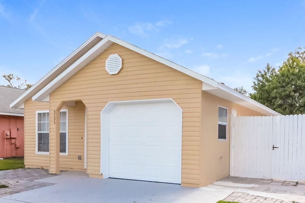 A tan, single-story house with a white garage door and a white wooden privacy fence — 9599 LUPINE AVENUE, ORLANDO, FL