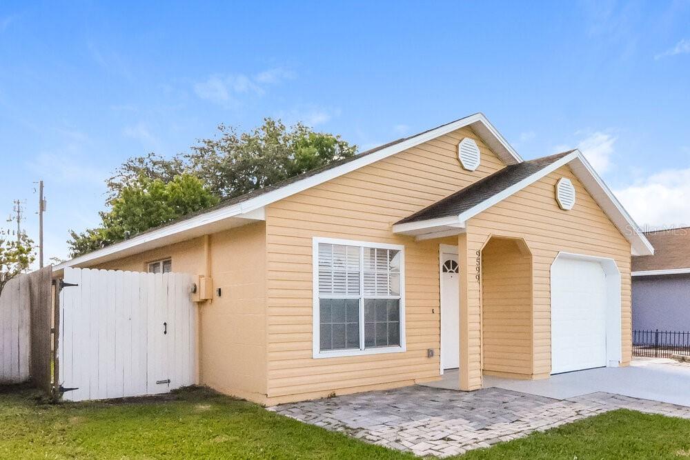 A single-story house with yellow siding, a white garage door, and a paved front patio — 9599 LUPINE AVENUE, ORLANDO, FL