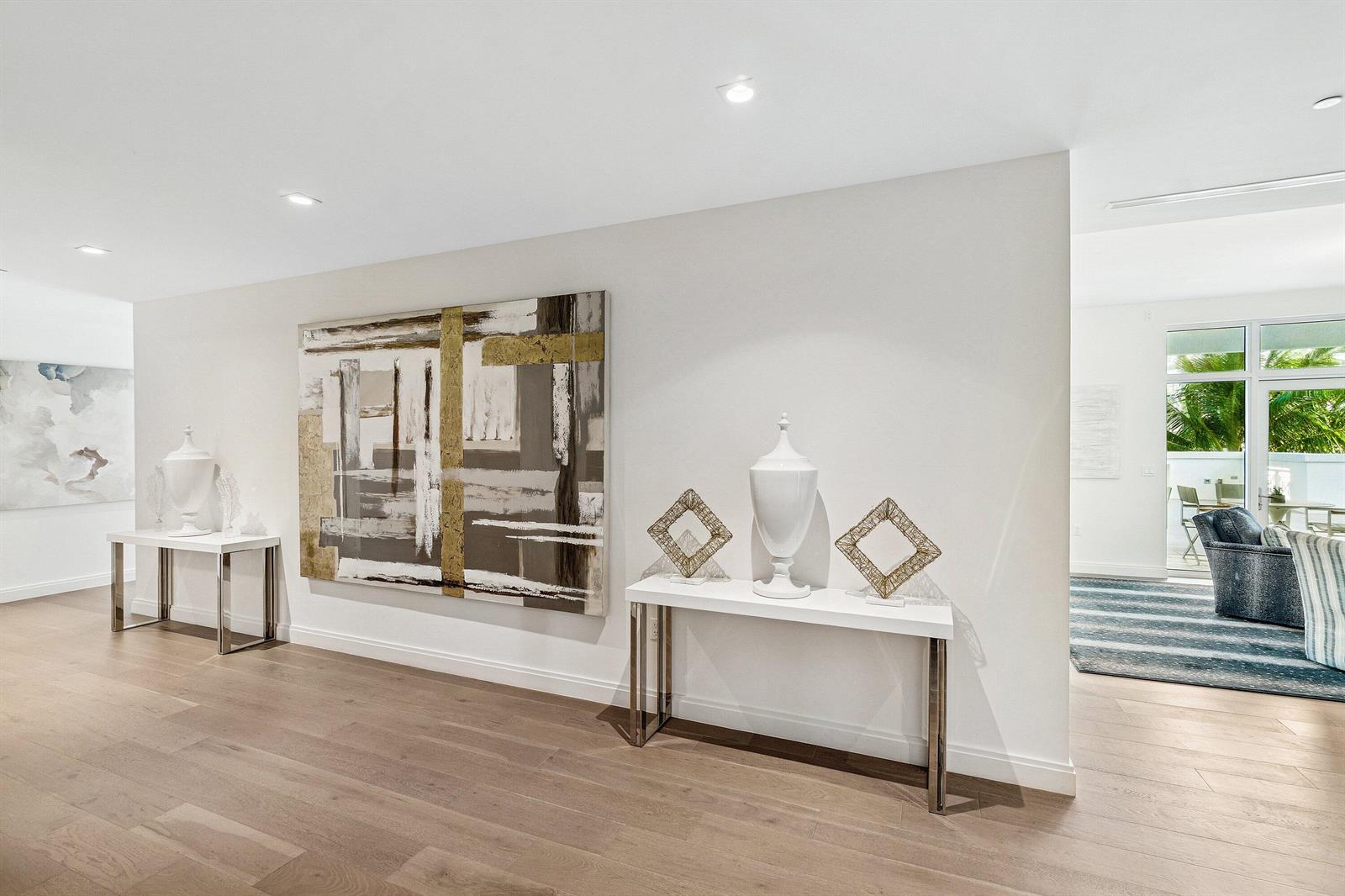 A hallway features light wood floors, two white console tables, and large abstract wall art — 3200 S Ocean Boulevard # 201, Highland Beach FL 33487, HIGHLAND BEACH, FL