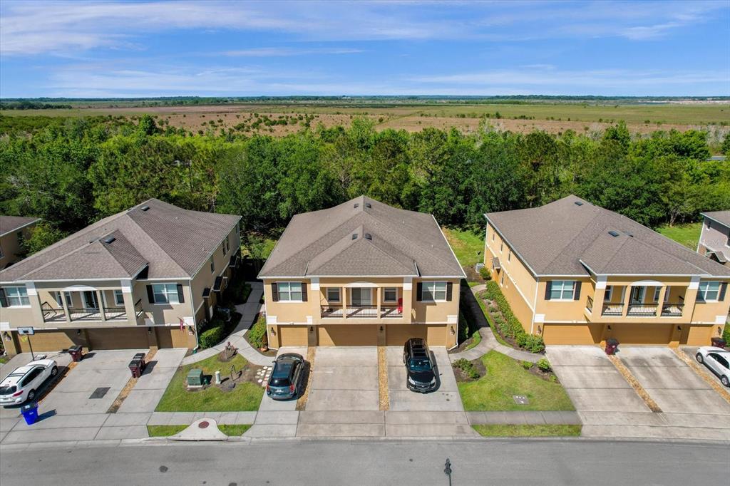 An aerial view shows three multi-story townhomes with driveways facing a street and wooded background — 2144 BETSY ROSS LANE, ST CLOUD, FL
