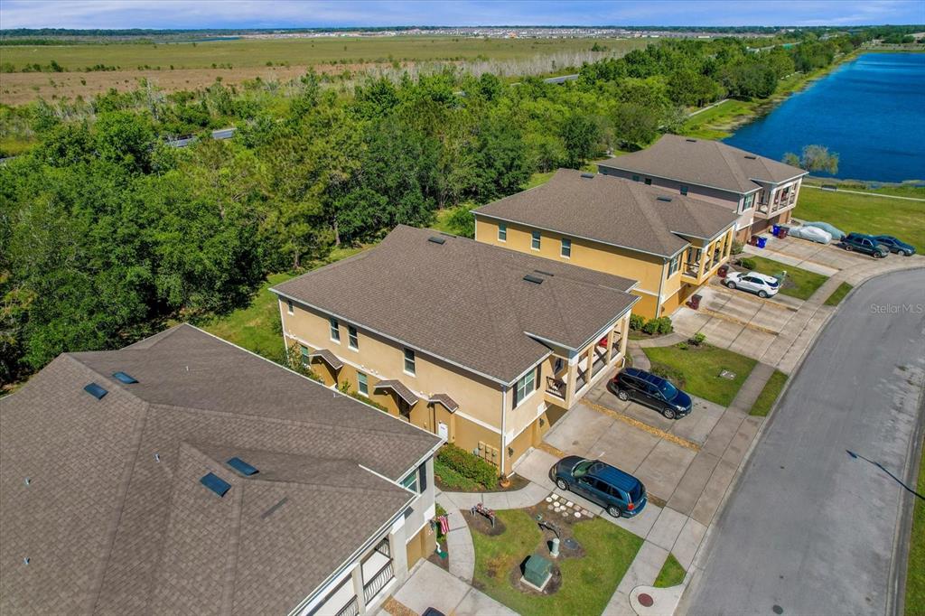 An aerial view shows several multi-story suburban townhomes with driveways next to a large pond — 2144 BETSY ROSS LANE, ST CLOUD, FL