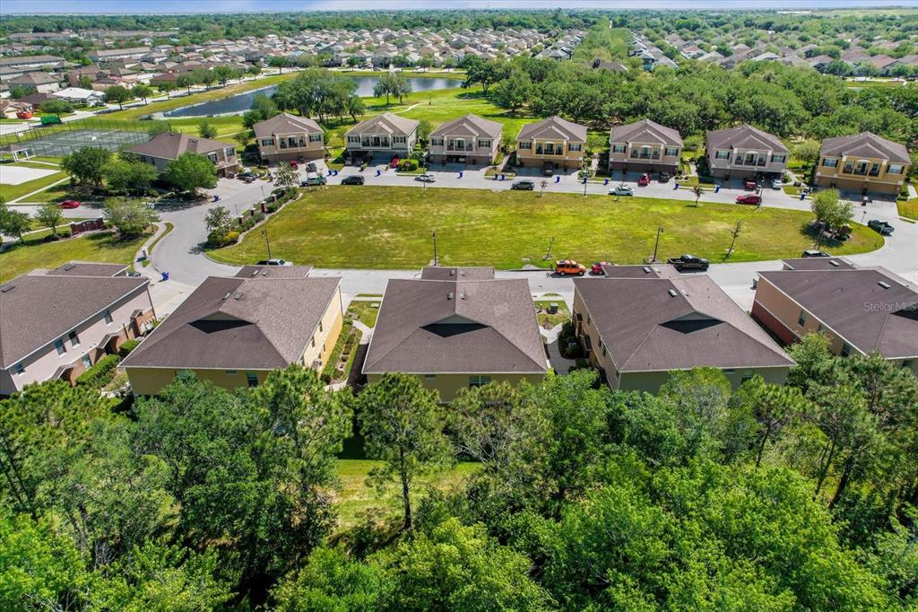 An aerial view shows a row of townhomes facing a large grassy lot and pond — 2144 BETSY ROSS LANE, ST CLOUD, FL