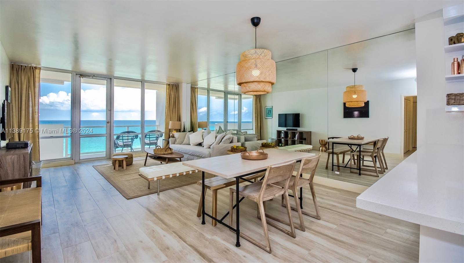 A bright living and dining area features light wood floors, a mirrored wall, and ocean views — 5601 Collins Ave # 1204, Miami Beach FL 33140, MIAMI BEACH, FL