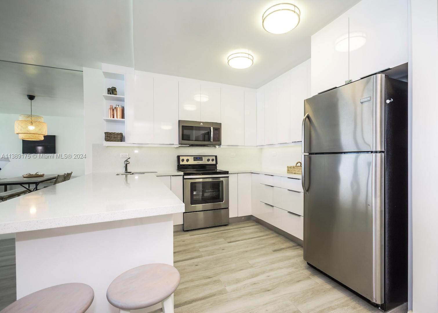 A modern kitchen features white cabinetry, stainless steel appliances, and a white quartz breakfast bar — 5601 Collins Ave # 1204, Miami Beach FL 33140, MIAMI BEACH, FL