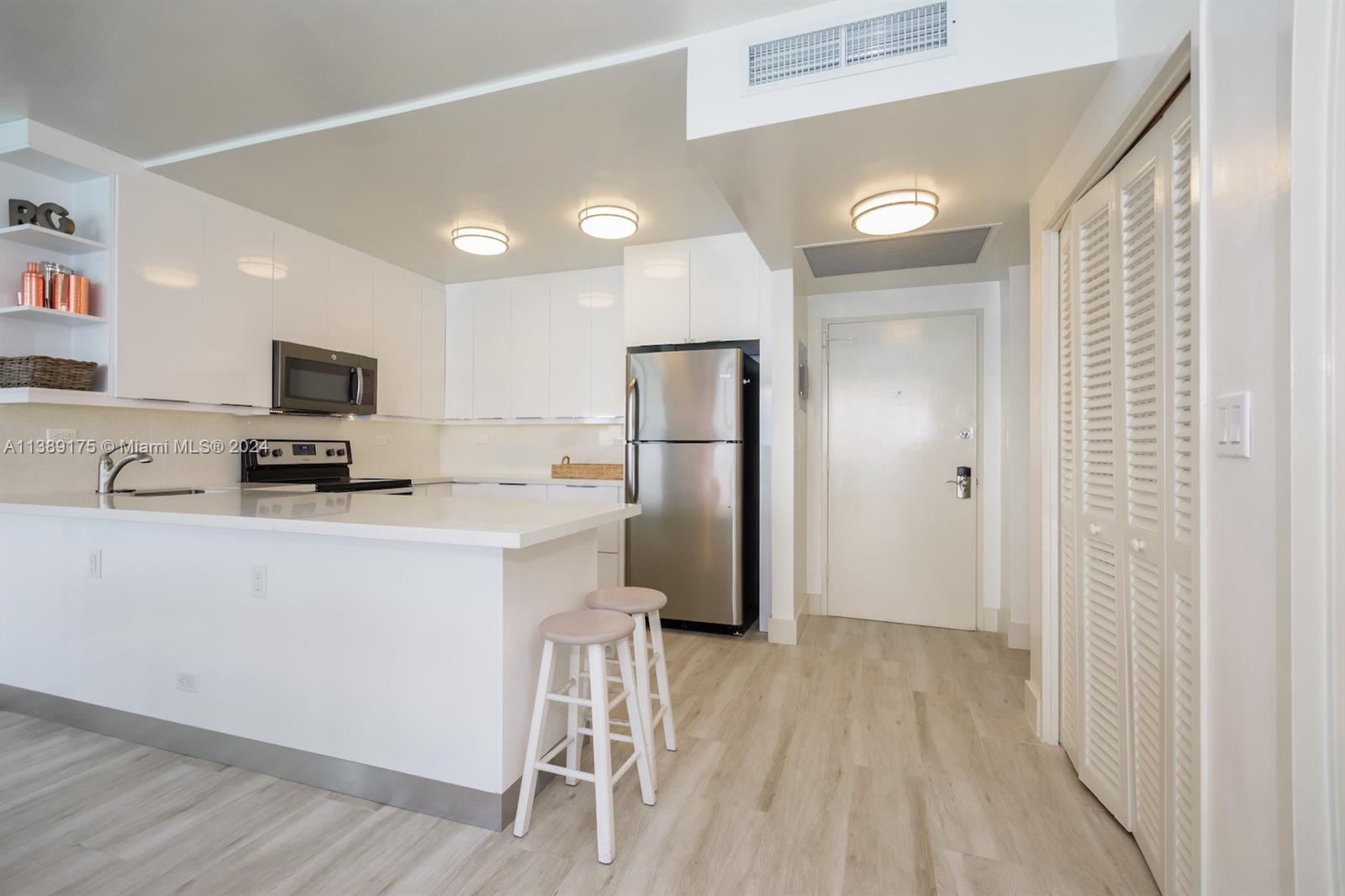 A modern kitchen features white cabinetry, stainless steel appliances, a breakfast bar, and light flooring — 5601 Collins Ave # 1204, Miami Beach FL 33140, MIAMI BEACH, FL