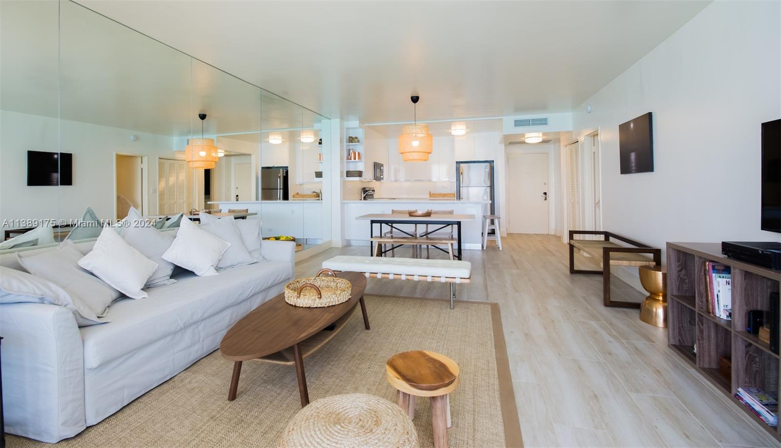 A living room and kitchen area features light wood flooring, a mirrored wall, and neutral furniture — 5601 Collins Ave # 1204, Miami Beach FL 33140, MIAMI BEACH, FL