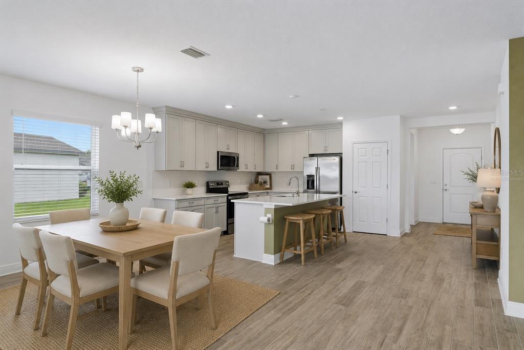 A kitchen and dining area features light wood floors, gray cabinets, and a kitchen island — 9959 LAST LIGHT GLEN, PARRISH, FL