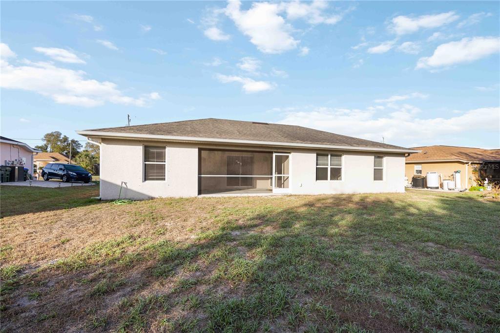 The rear exterior of a single-story house features a screened-in porch and a grassy yard — 1698 N LAVINA STREET, NORTH PORT, FL