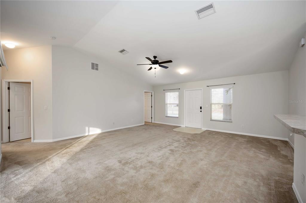A spacious living room with beige carpeting, vaulted ceilings, a ceiling fan, and a front door — 1698 N LAVINA STREET, NORTH PORT, FL