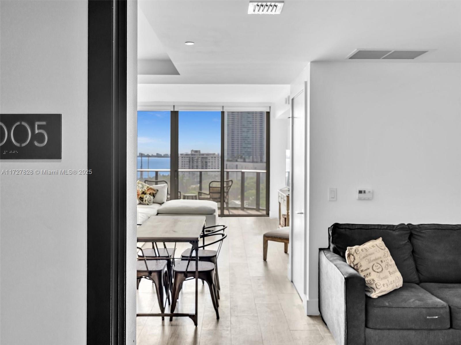 A bright living area features a dining set, a gray sofa, and a balcony view — 121 NE 34th St # 1005, Miami FL 33137, MIAMI, FL