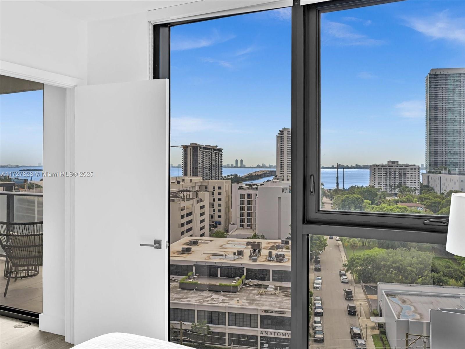 A bedroom window offers a view of city buildings, a street, and the ocean — 121 NE 34th St # 1005, Miami FL 33137, MIAMI, FL