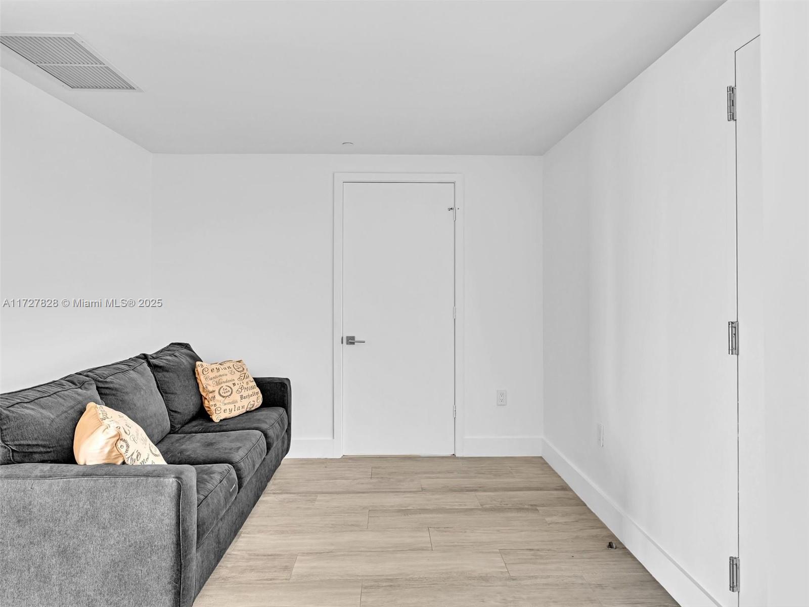 A gray sofa sits in a room with white walls and light wood-look flooring — 121 NE 34th St # 1005, Miami FL 33137, MIAMI, FL