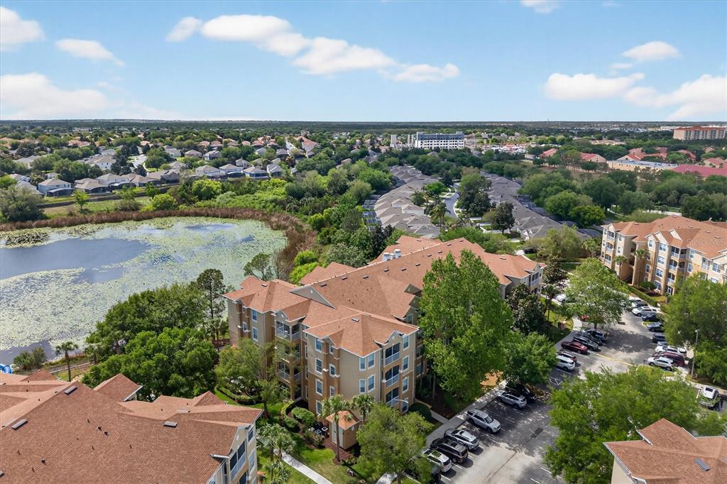 An aerial view shows multi-story apartment buildings, a large pond, and a parking lot — 7664 COMROW STREET UNIT 304, KISSIMMEE, FL