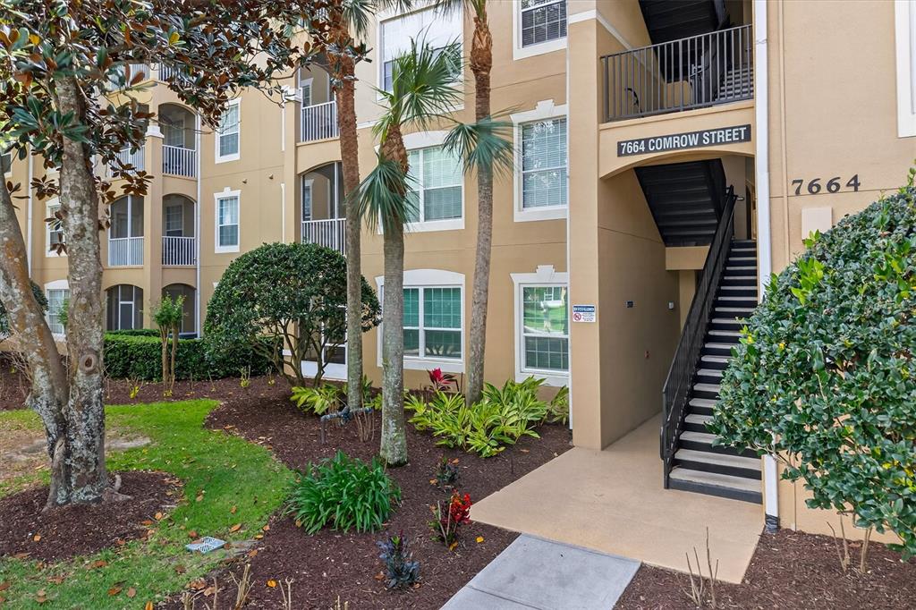 An exterior view of a multi-story apartment building with a staircase and palm trees — 7664 COMROW STREET UNIT 304, KISSIMMEE, FL