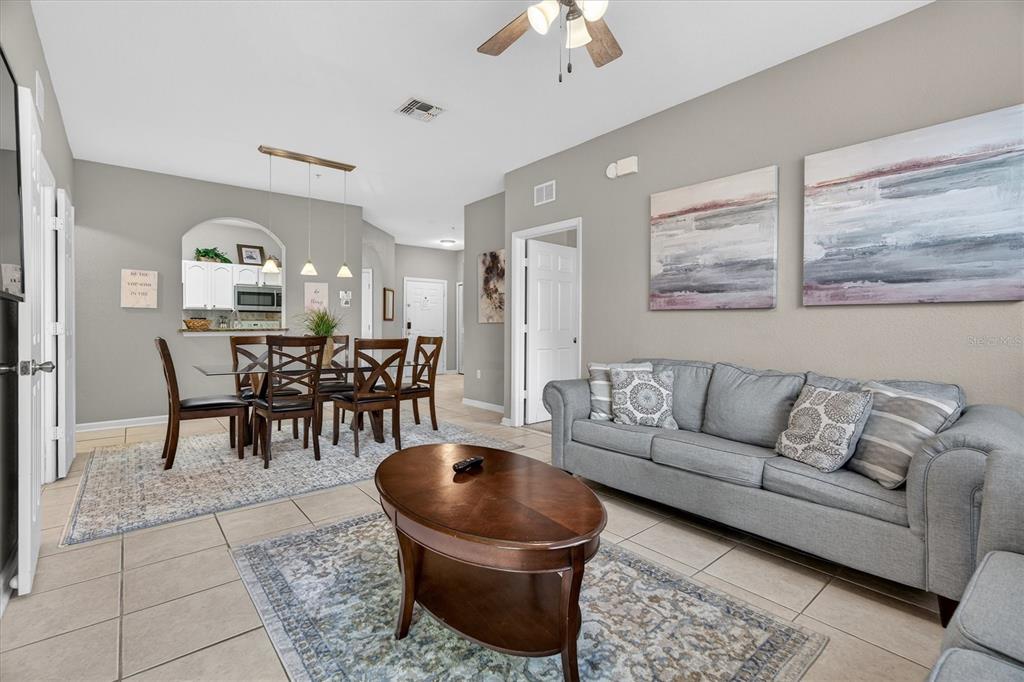 A living room and dining area feature tile floors, a gray sofa, and neutral walls — 7664 COMROW STREET UNIT 304, KISSIMMEE, FL