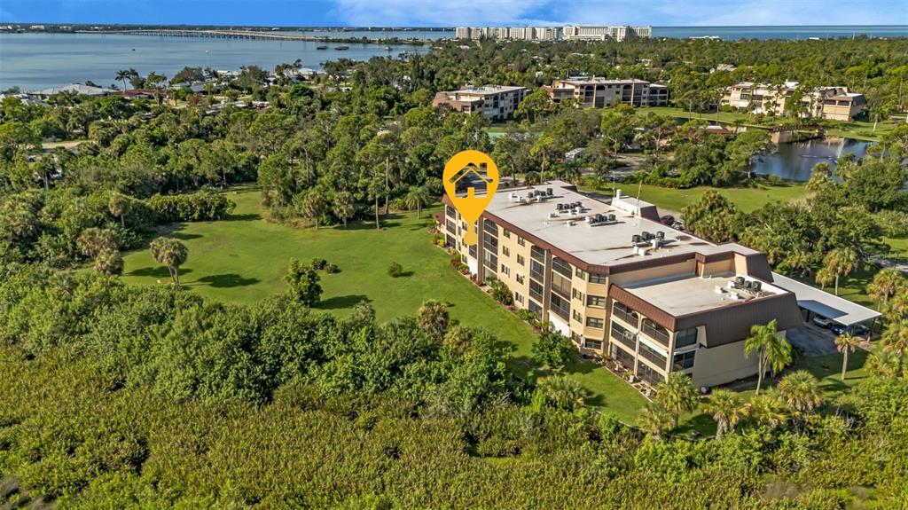 An aerial view shows a multi-story apartment building surrounded by trees and a grassy lawn — 23465 HARBORVIEW ROAD UNIT 225, PUNTA GORDA, FL