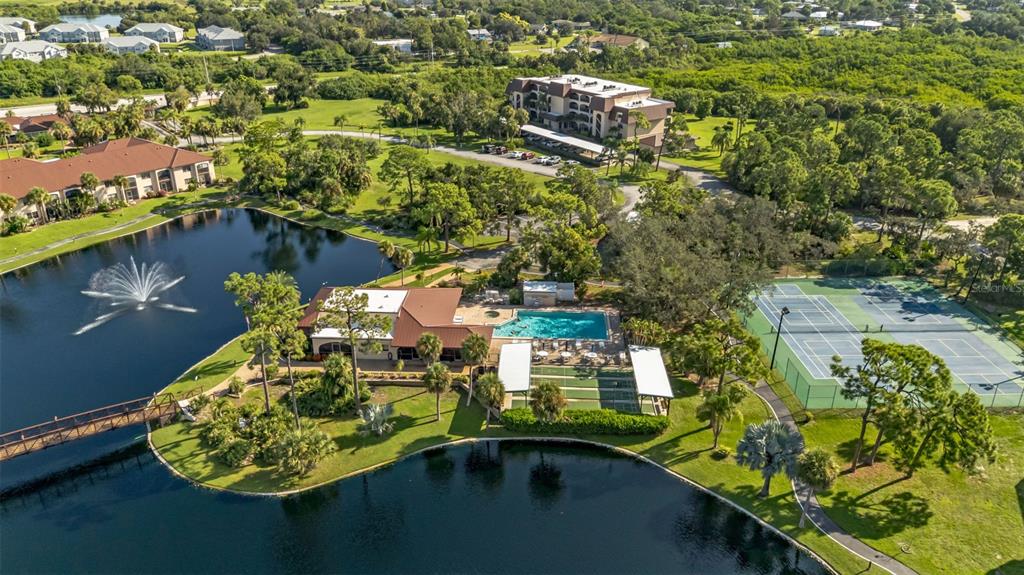 Aerial view of a community clubhouse with a pool, tennis courts, and a lake fountain — 23465 HARBORVIEW ROAD UNIT 225, PUNTA GORDA, FL