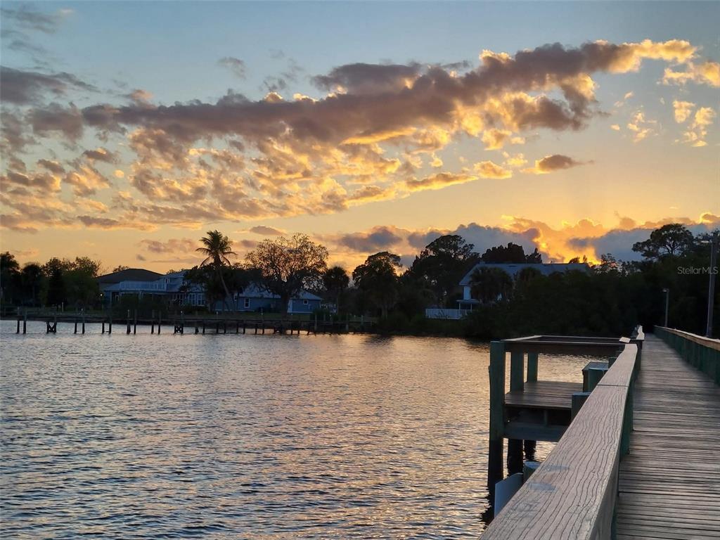 A wooden pier extends over calm water toward houses under a sunset sky — 23465 HARBORVIEW ROAD UNIT 225, PUNTA GORDA, FL