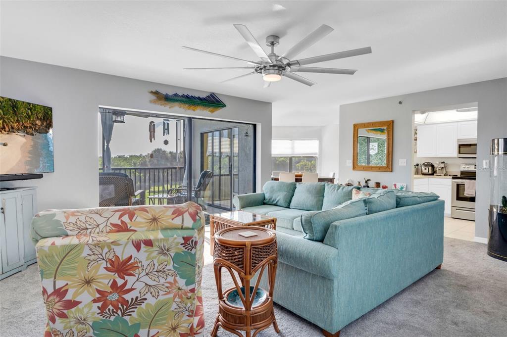 A living room features a teal sectional sofa, floral armchair, ceiling fan, and sliding glass doors — 23465 HARBORVIEW ROAD UNIT 225, PUNTA GORDA, FL