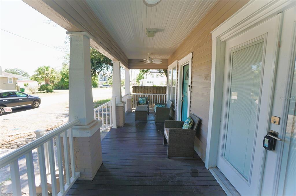 A covered wooden front porch features white railings, wicker furniture, and a ceiling fan — 2511 W FIG STREET, TAMPA, FL