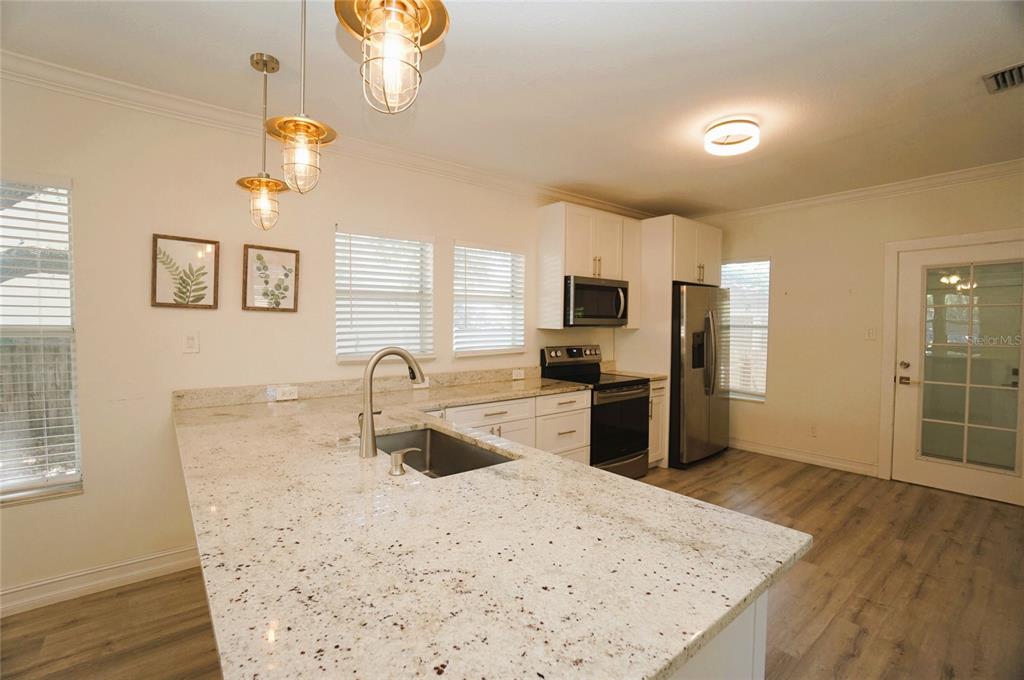 A kitchen features a granite island with a sink, white cabinets, and stainless steel appliances — 2511 W FIG STREET, TAMPA, FL