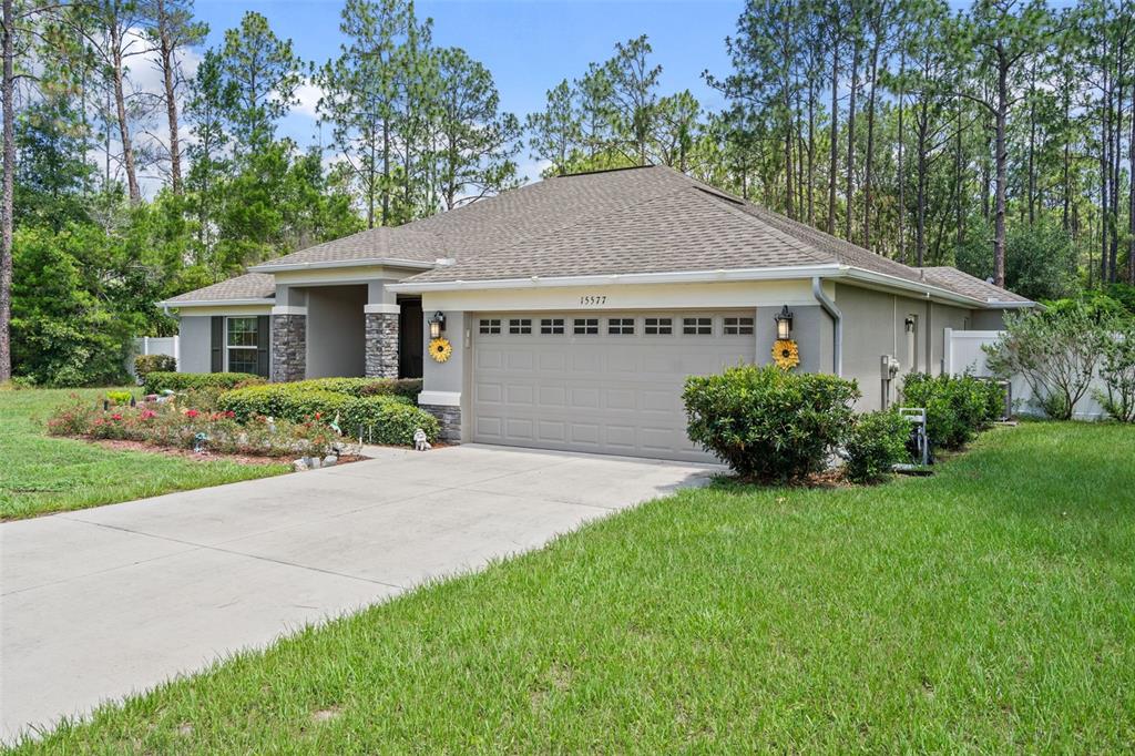 A single-story house with a beige stucco exterior, a two-car garage, and a landscaped yard — 15577 SAGO DRIVE, BROOKSVILLE, FL